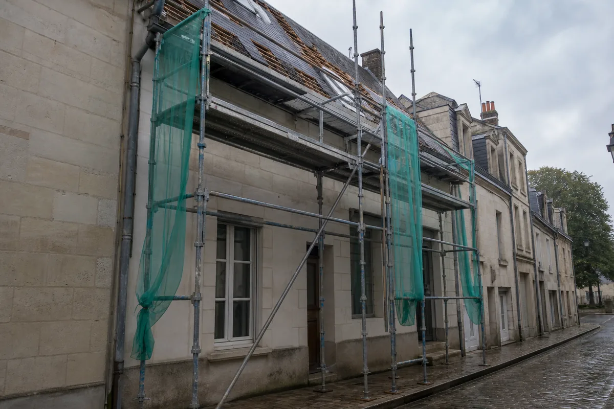 Échafaudage dressé sur le trottoir devant une maison de bourg mitoyenne en calcaire clair