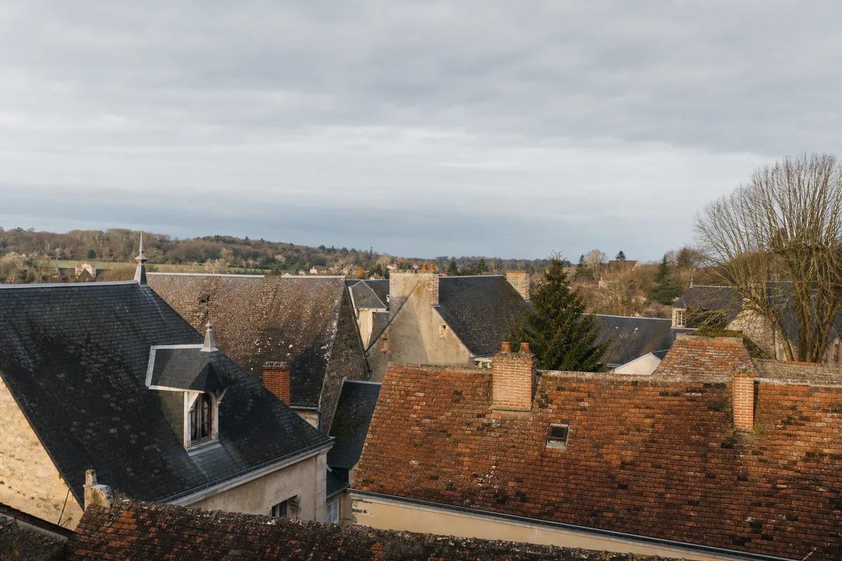 Toits d&rsquo;ardoise et de tuile brune se succédant sur un bourg sarthois sous un ciel gris perle